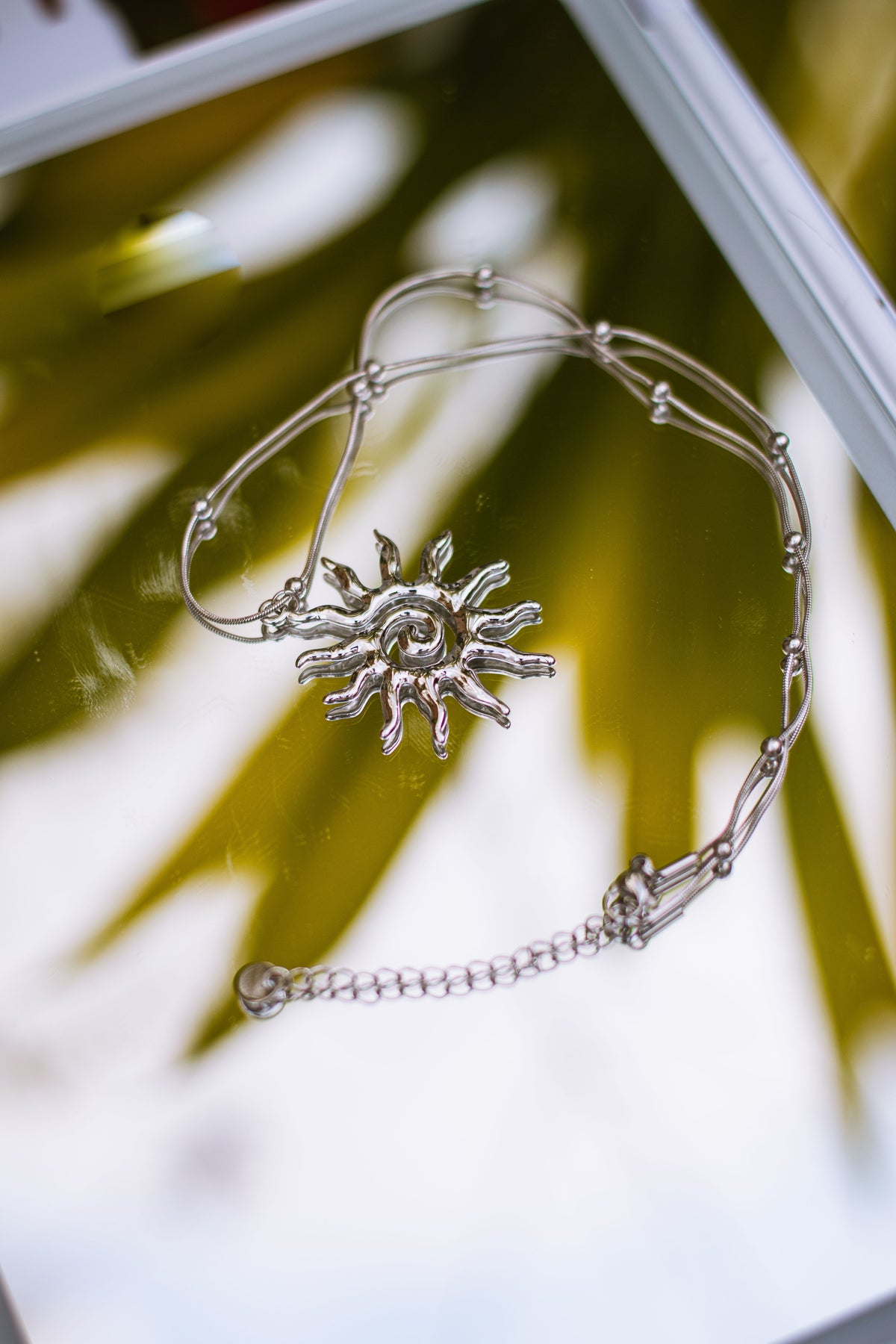 Silver sun charm necklace on mirror